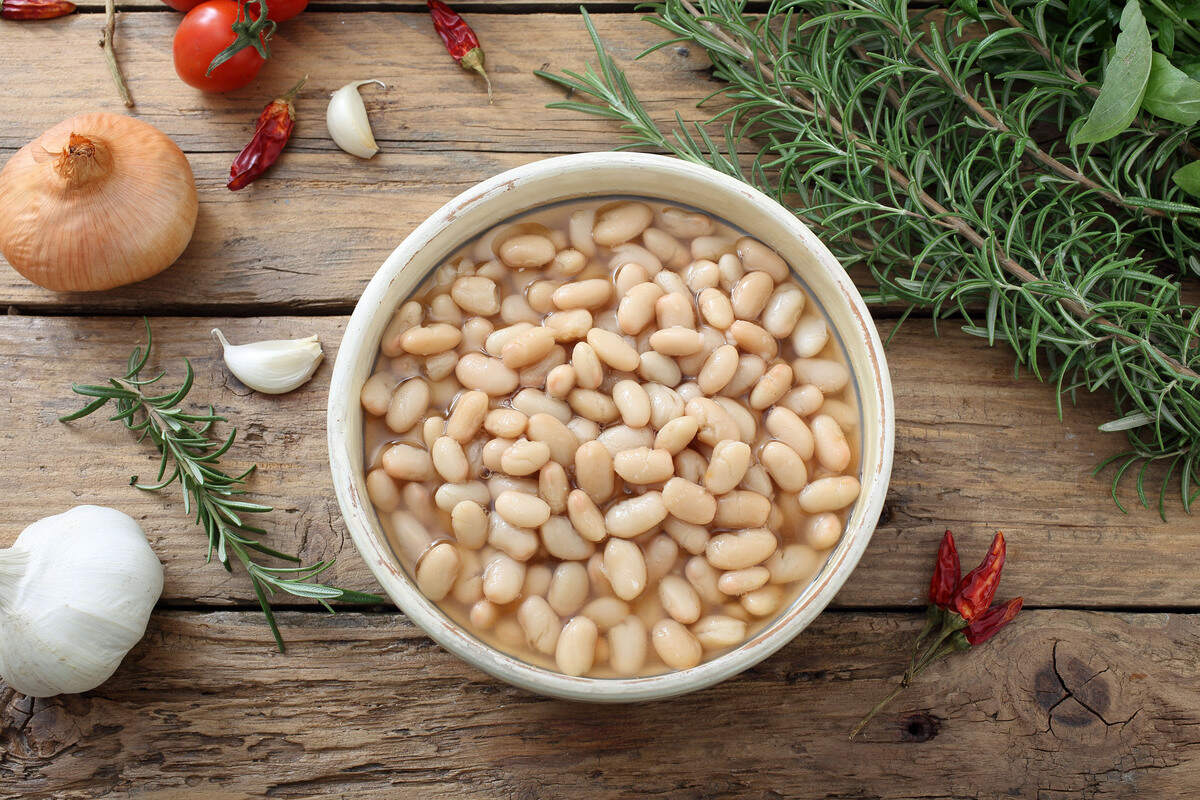 Vista dall'alto ciotola con fagioli cannellini cotti e attorno cipolla, aglio, rosmarino e peperoncino