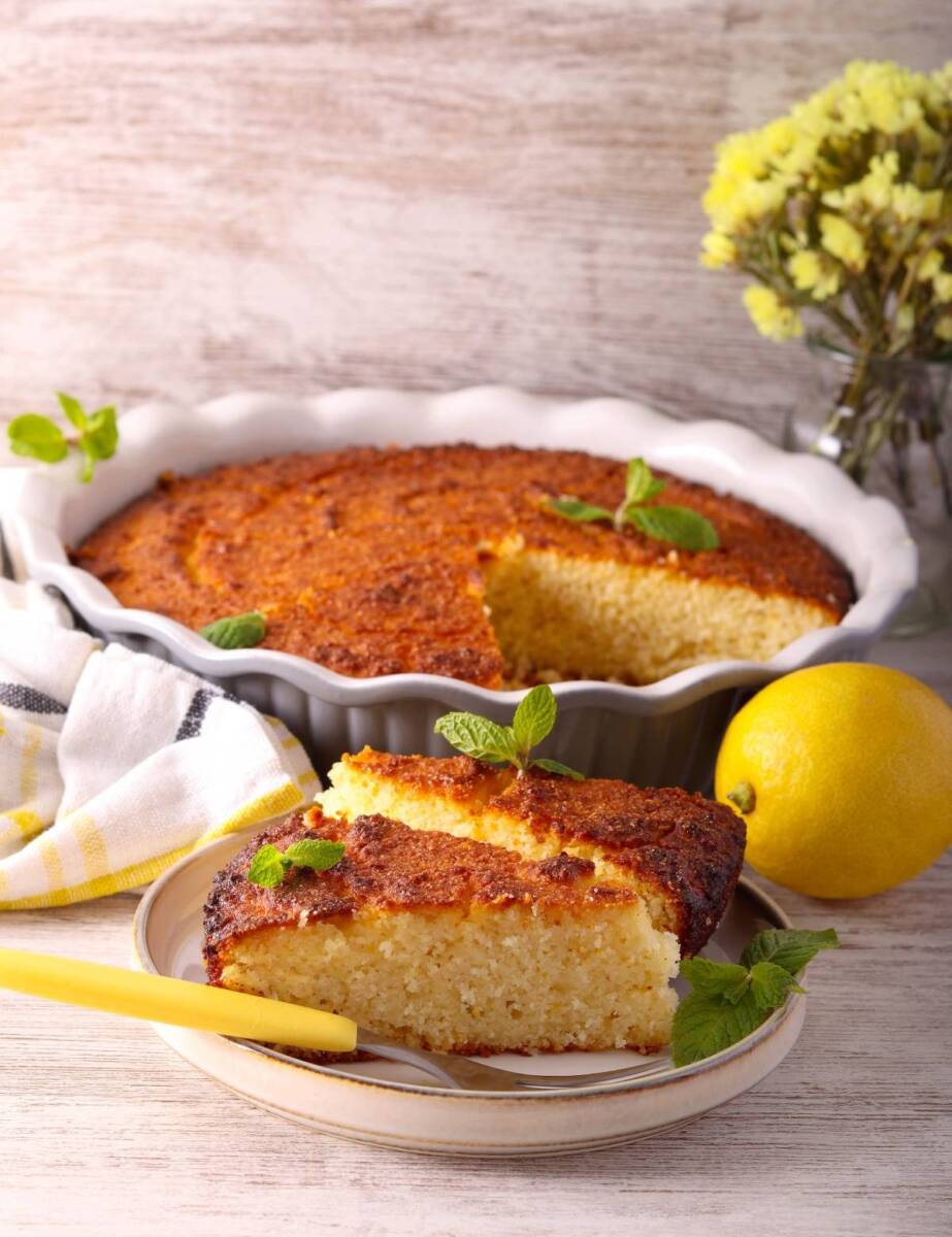 Tortiera in ceramica con torta al limone da cui manca una fetta in primo piano su piatto