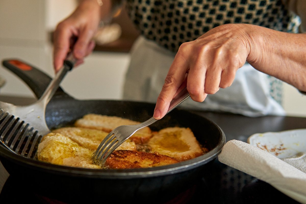 Mani di donna che girano in padella pane fritto tipo torrijas 