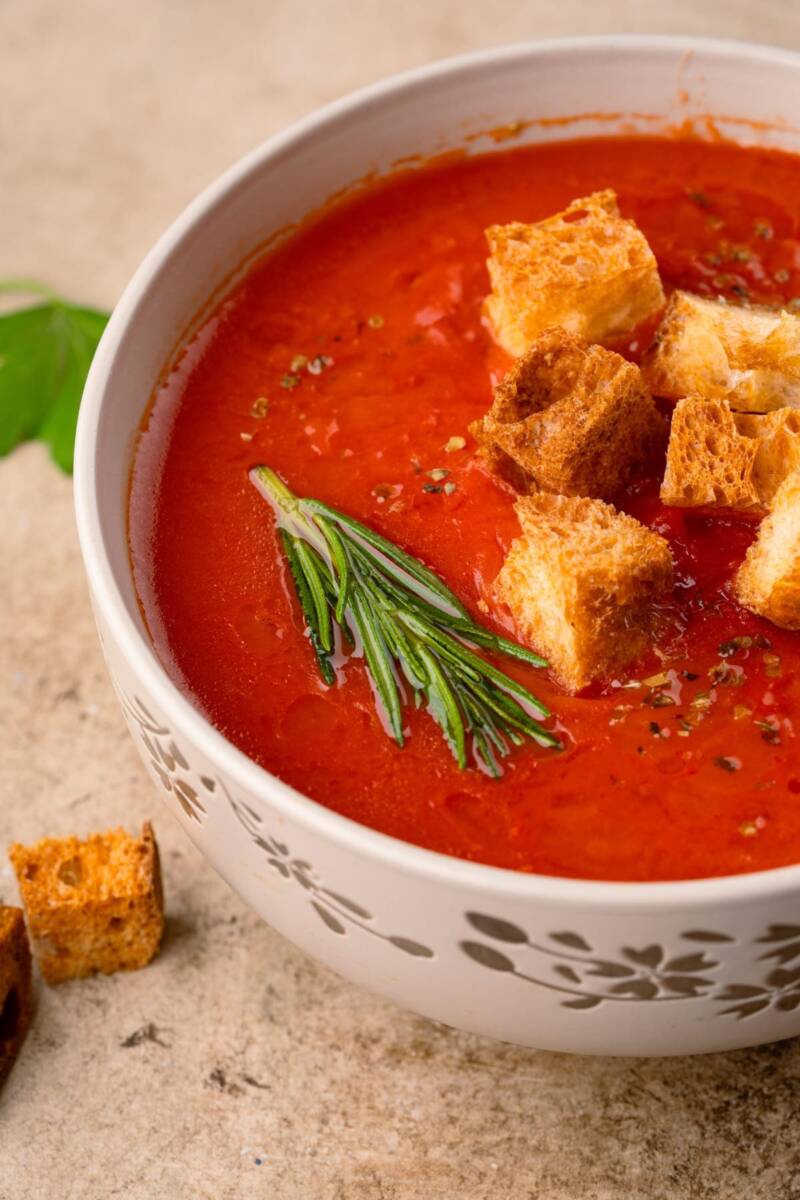 Ciotola con zuppa di pomodoro decorata con rosmarino e crostini di pane