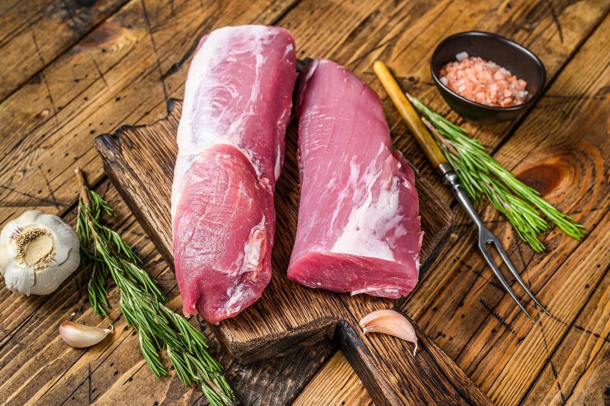 Filetti di maiale ancora da cuocere su tagliere con erbe aromatiche e aglio