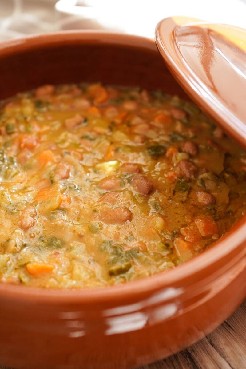 Pentola in terracotta con coperchio spostato contenenze zuppa di fagioli, cavolo nero e farina di mais