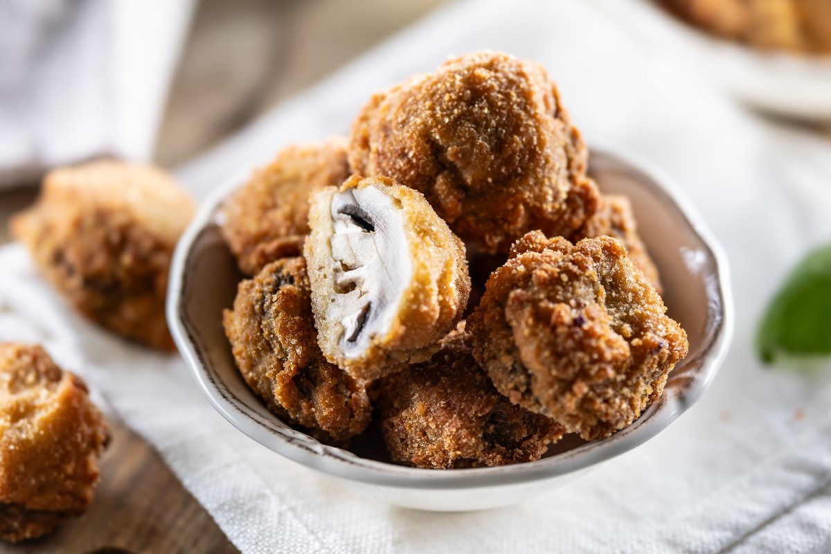 Ciotola di ceramica con funghi champignon impanati e fritti uno dei quali tagliato a metà