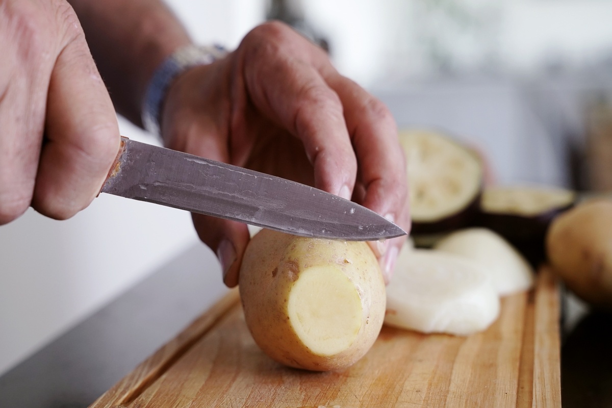 Mani che riducono le patate a fette su tagliere di legno