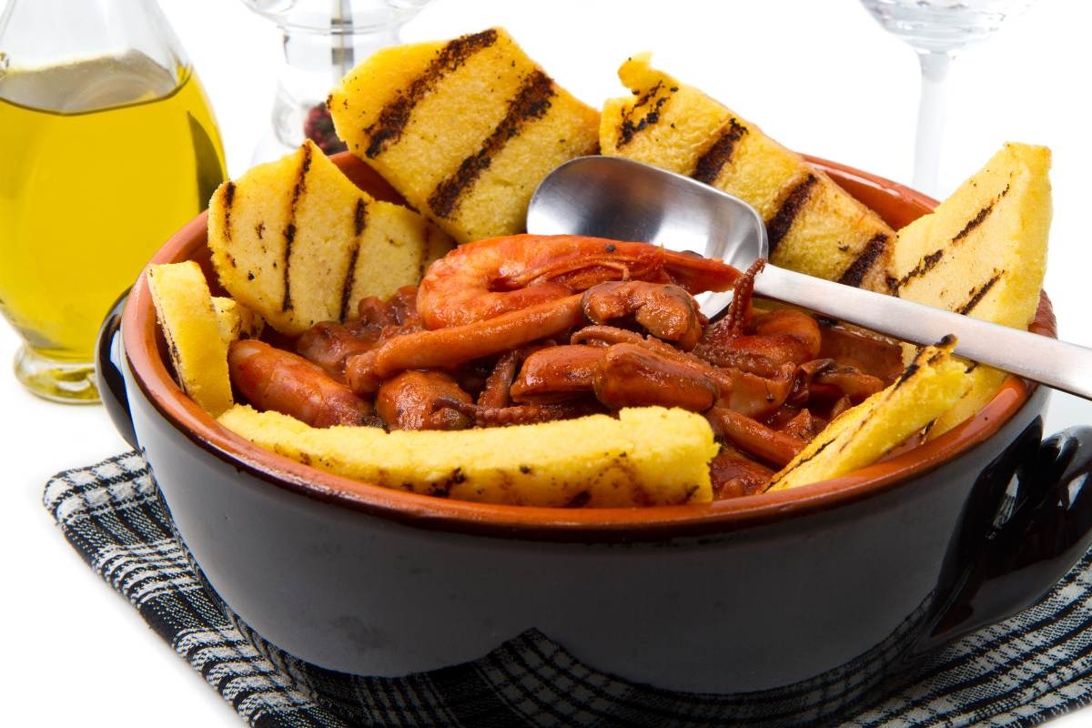 Tegame in terracotta con zuppa di pesce e crostini di polenta