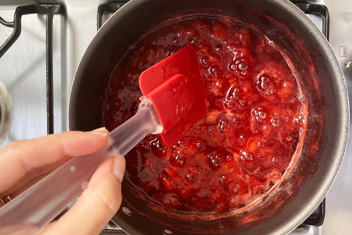Vista dall'alto mano che mescola con leccapentola marmellata di fragole in cottura