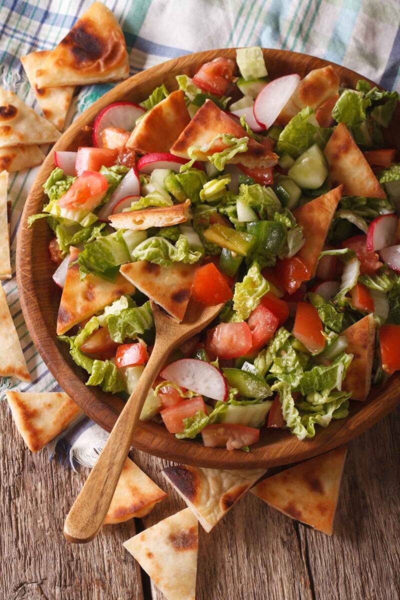 Vista dall'alto ciotola di legno con insalata di lattuga, pomodori, cetrioli e crostini di pane pita