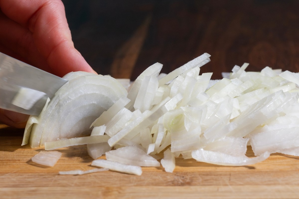 Mani che riducono a fette cipolle su tagliere di legno