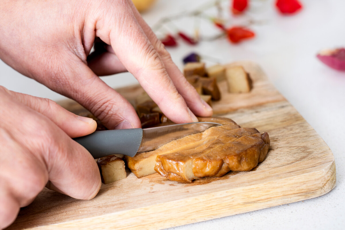 Mani che tagliano panetto di seitan a fette