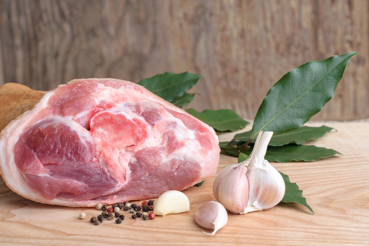 Stinco di maiale crudo su tagliere di legno con pepe, aglio e alloro