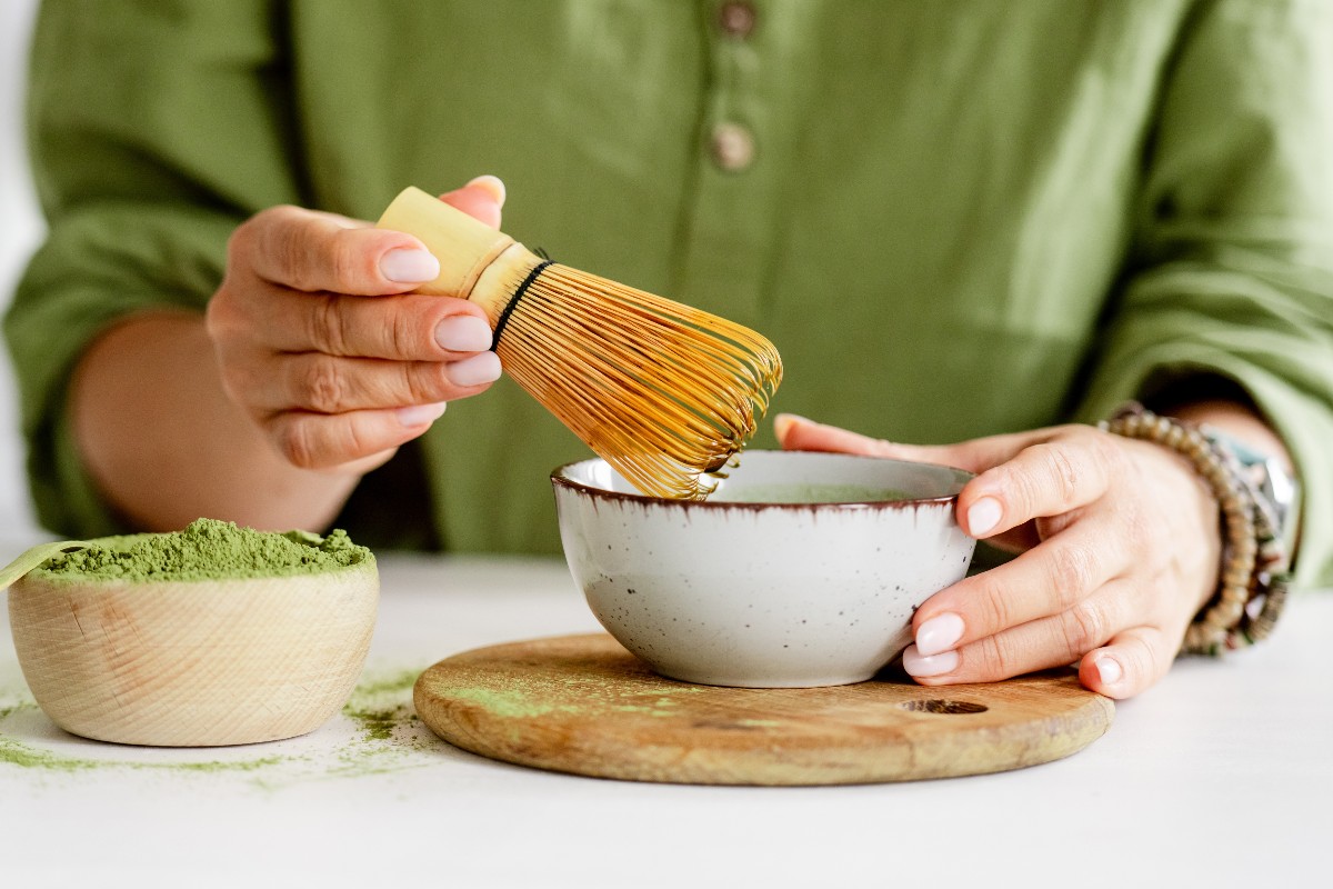 Donna sullo sfondo che mescola tè matcha in polvere con apposito frustino in bambù