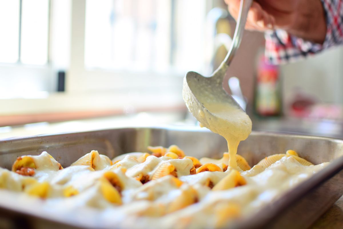 Salsa besciamella versata su teglia di pasta al forno con cucchiaio