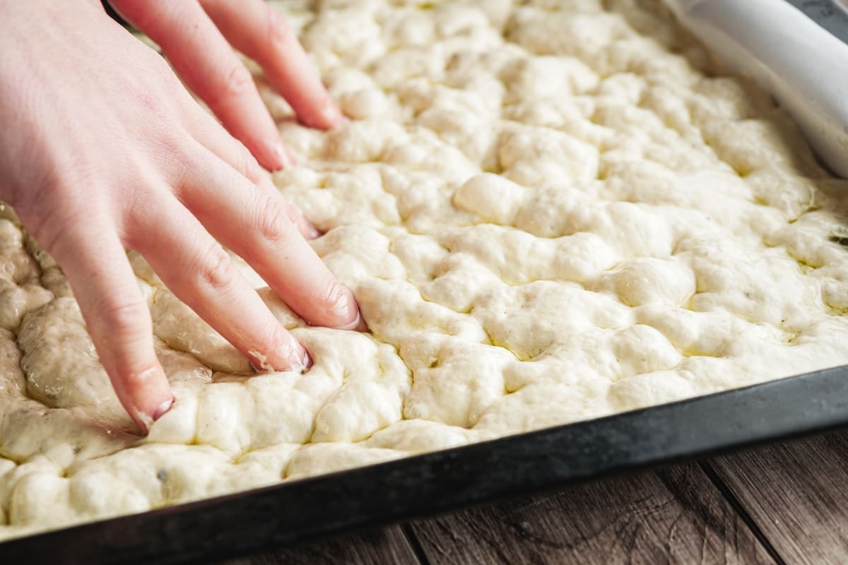 Mani che stendono focaccia nella teglia