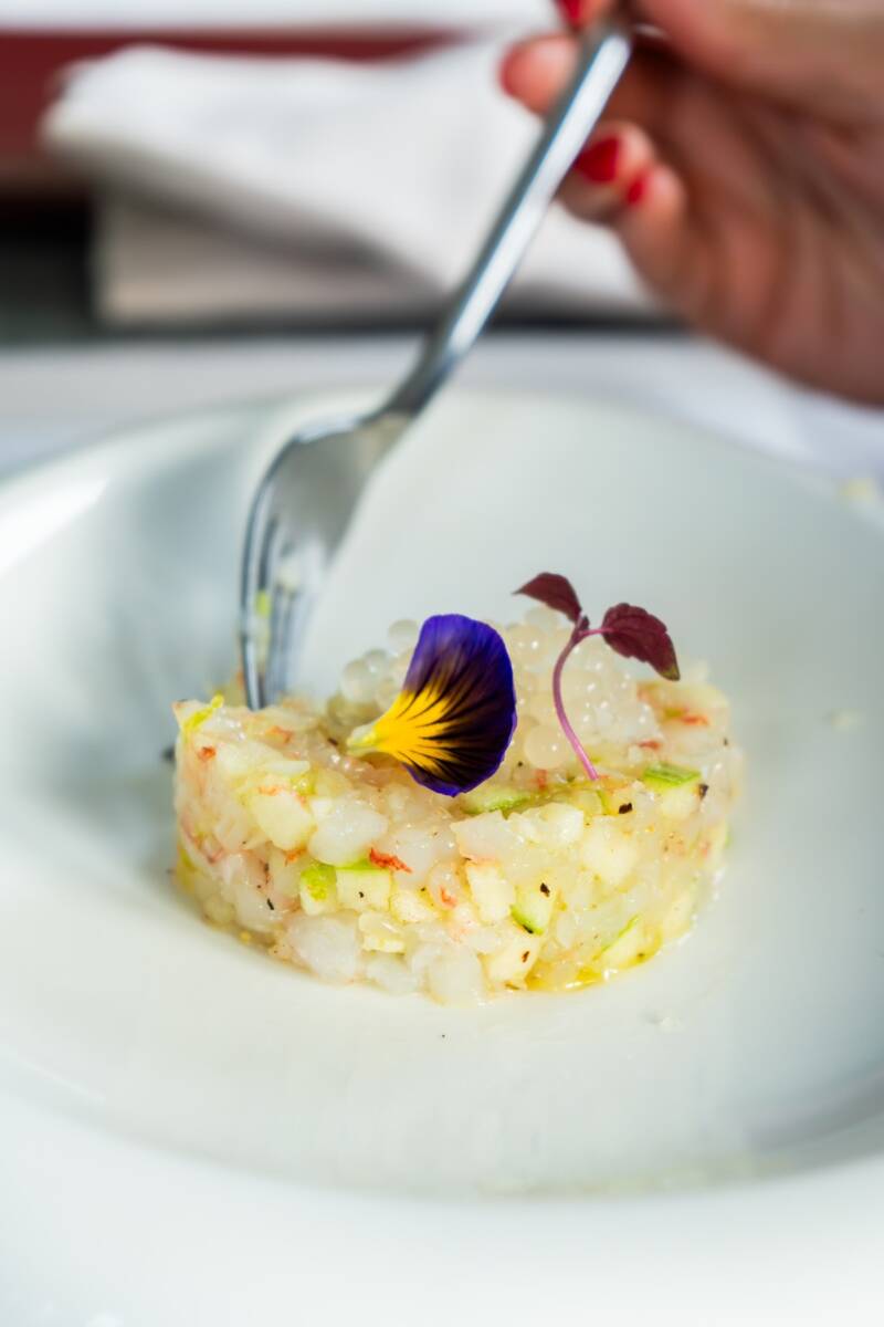 Forchetta tenuta da mano di donna che prende porzione di tartare di pesce dal piatto
