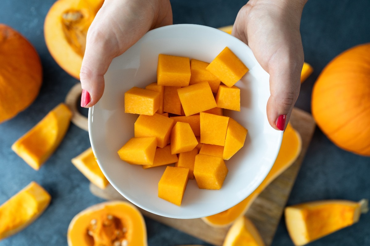 Vista dall'alto mani di donna che tengono una ciotola con zucca tagliata a cubetti