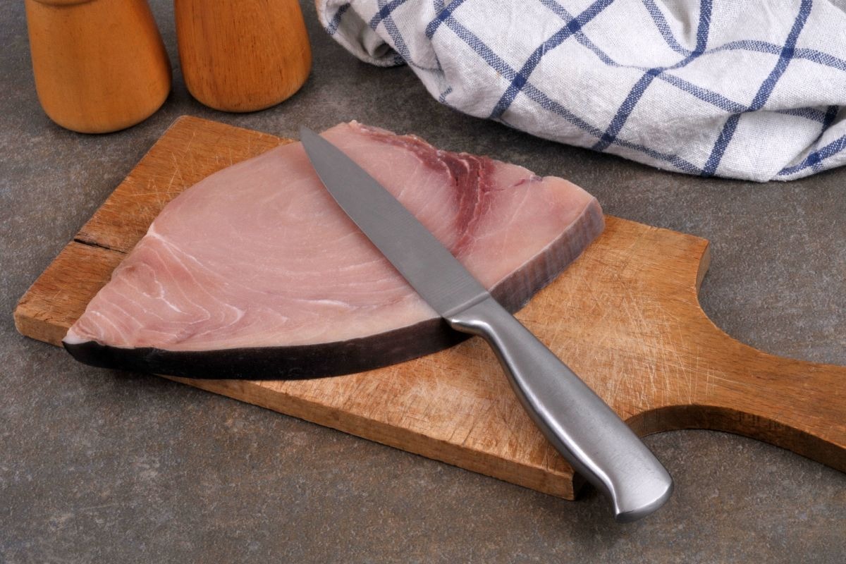 Tagliere di legno con trancio di pesce spada e coltello