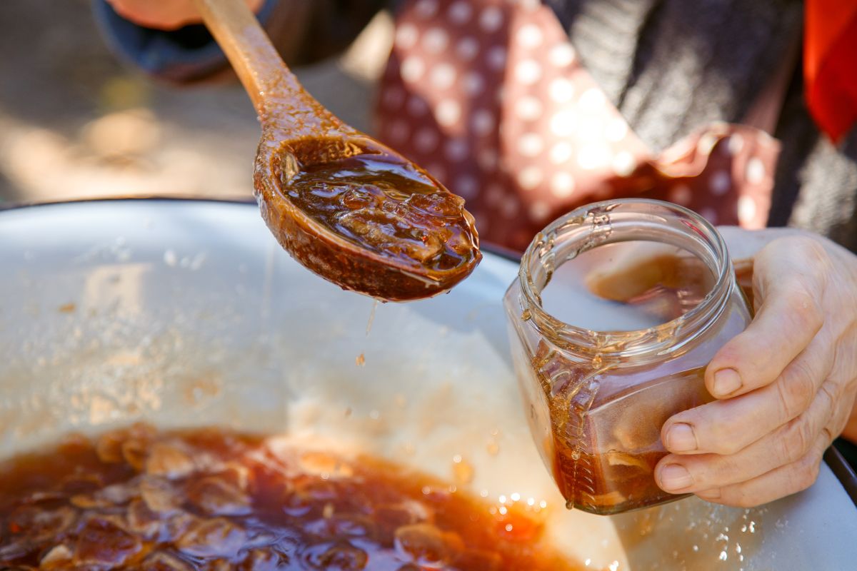 Atto di versare la marmellata nei vasetti con cucchiaio di legno