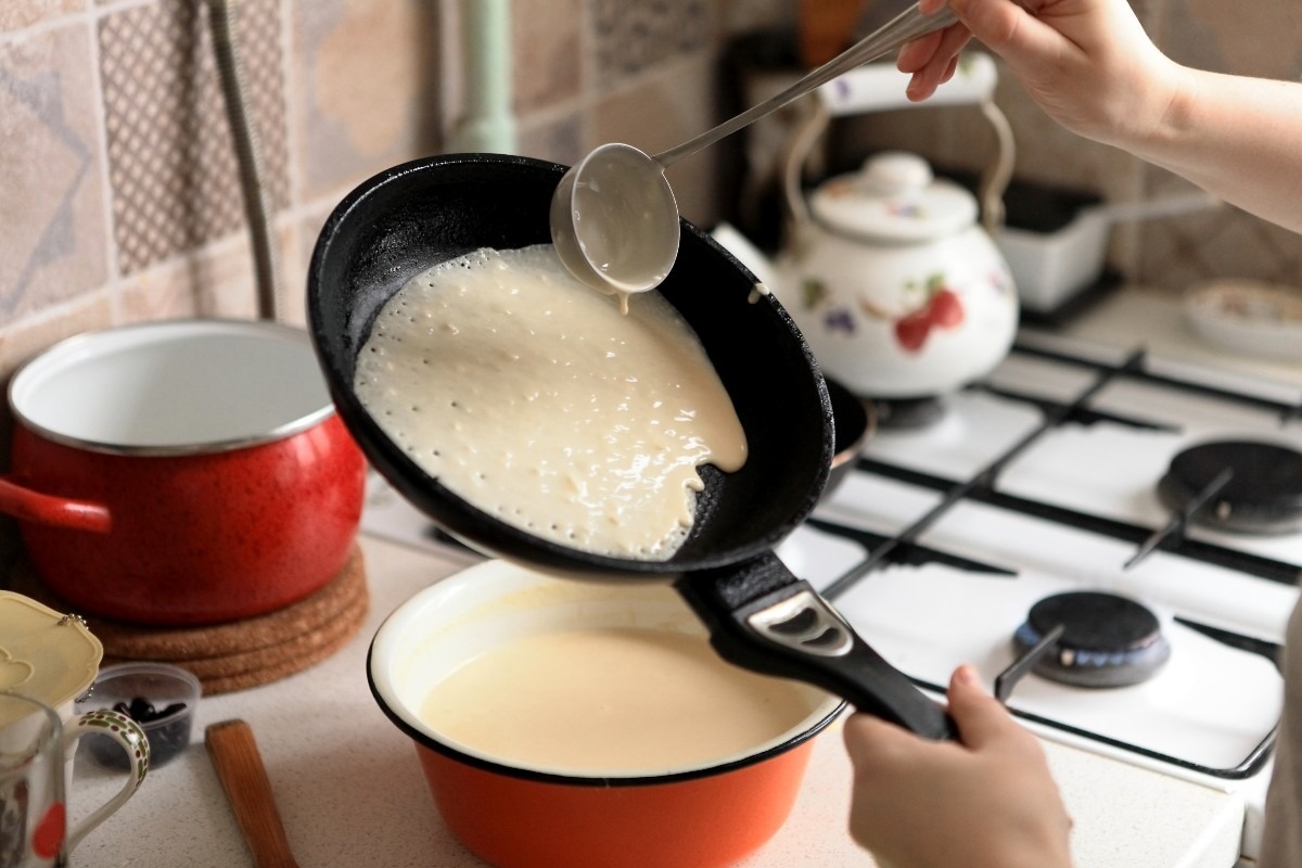Mani di donna che preparano le crêpes versando pastella in padella antiaderente
