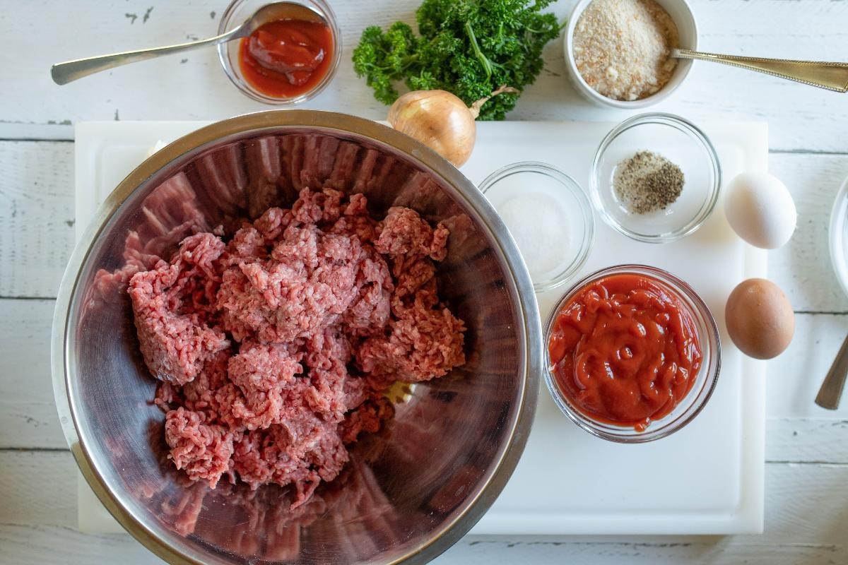 Vista dall'alto ingredienti per preparazione polpettone: carne macinata, uova, prezzemolo, formaggio e passata di pomodoro
