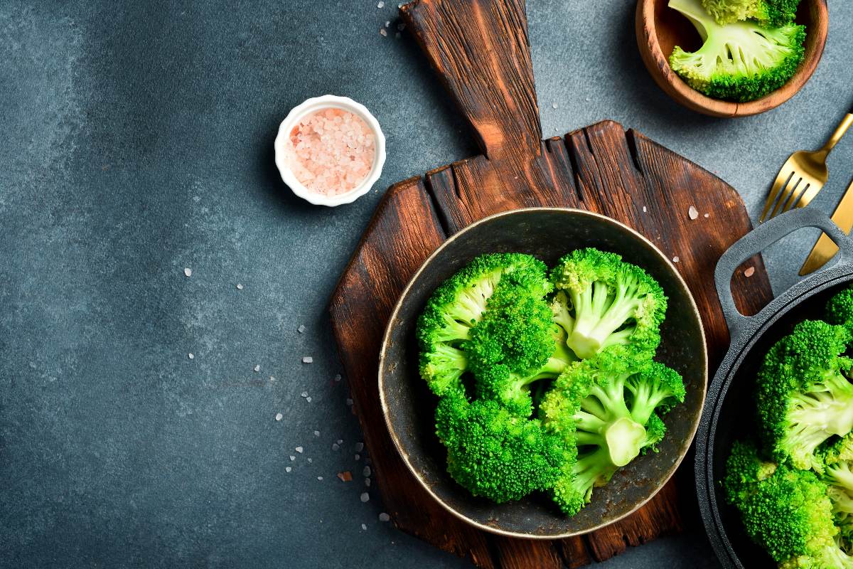 Vista dall'alto broccoli cotti in ciotola su tagliere di legno