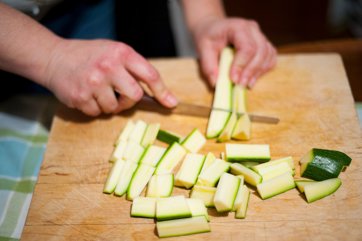 Donna che taglia a strisce le zucchine su tagliere di legno