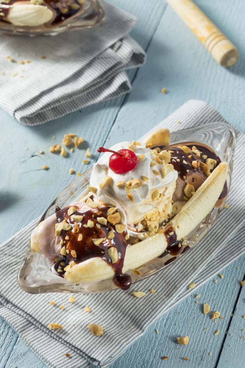 Piatto a barchetta con banana tagliata a metà, gelato, panna, topping al cioccolato, panna e amarena