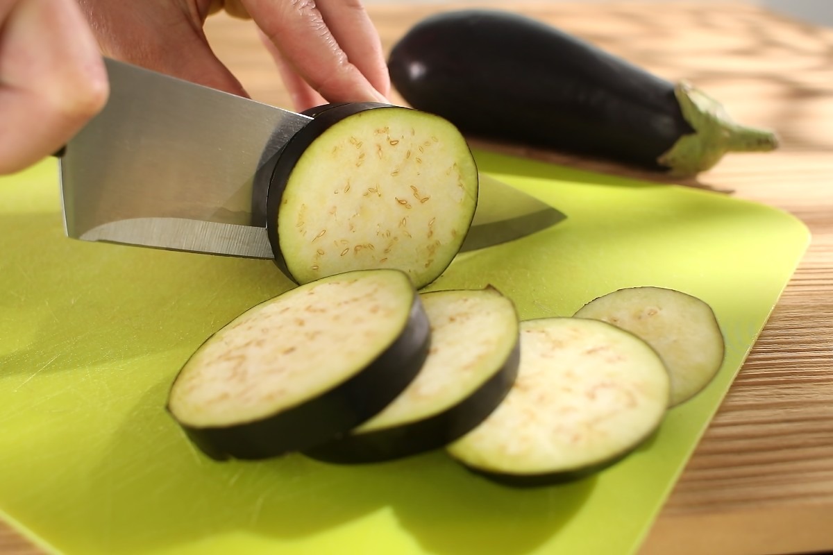 Mano che taglia a fette le melanzane con coltello su tagliere verde