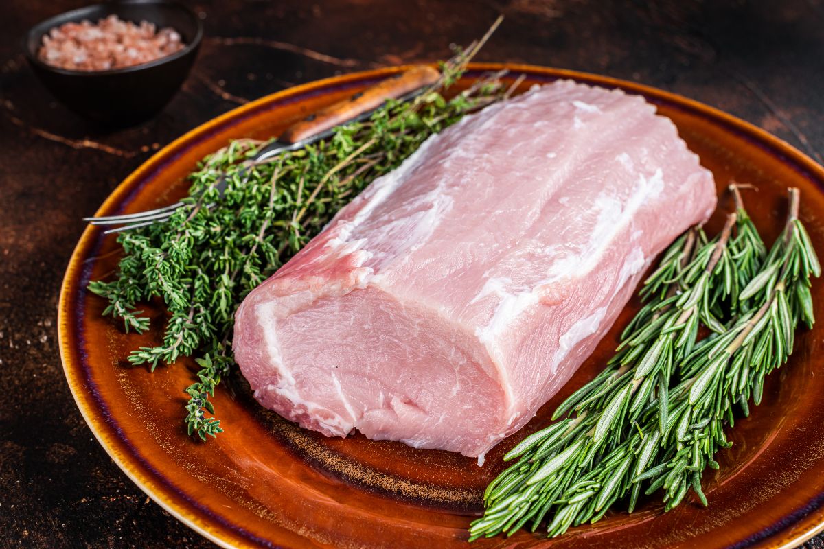 Arista, lonza, lombo o lombata di maiale cruda su piatto con rosmarino e timo