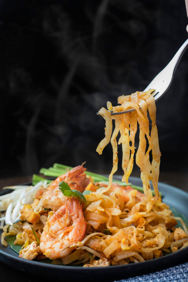 Forchetta che solleva pasta pad thai con gamberi dal piatto 