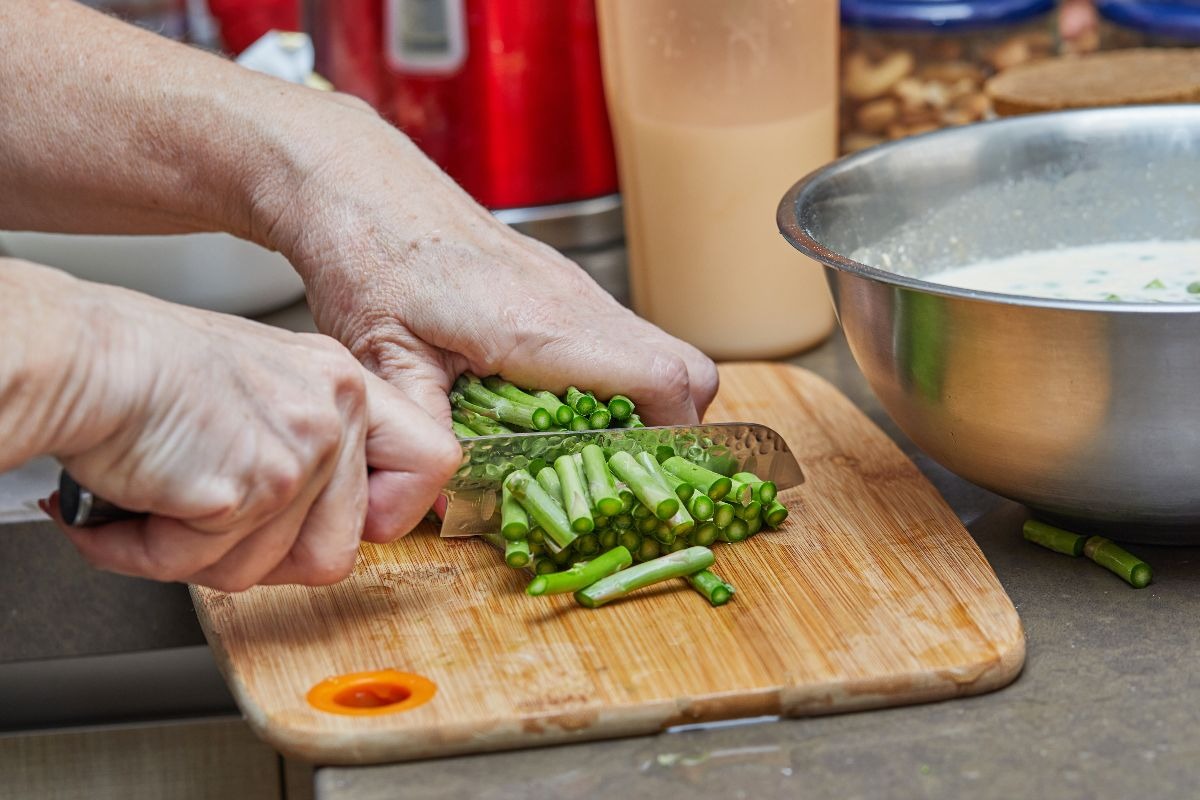 Mani che tagliano asparagi su tagliere di legno