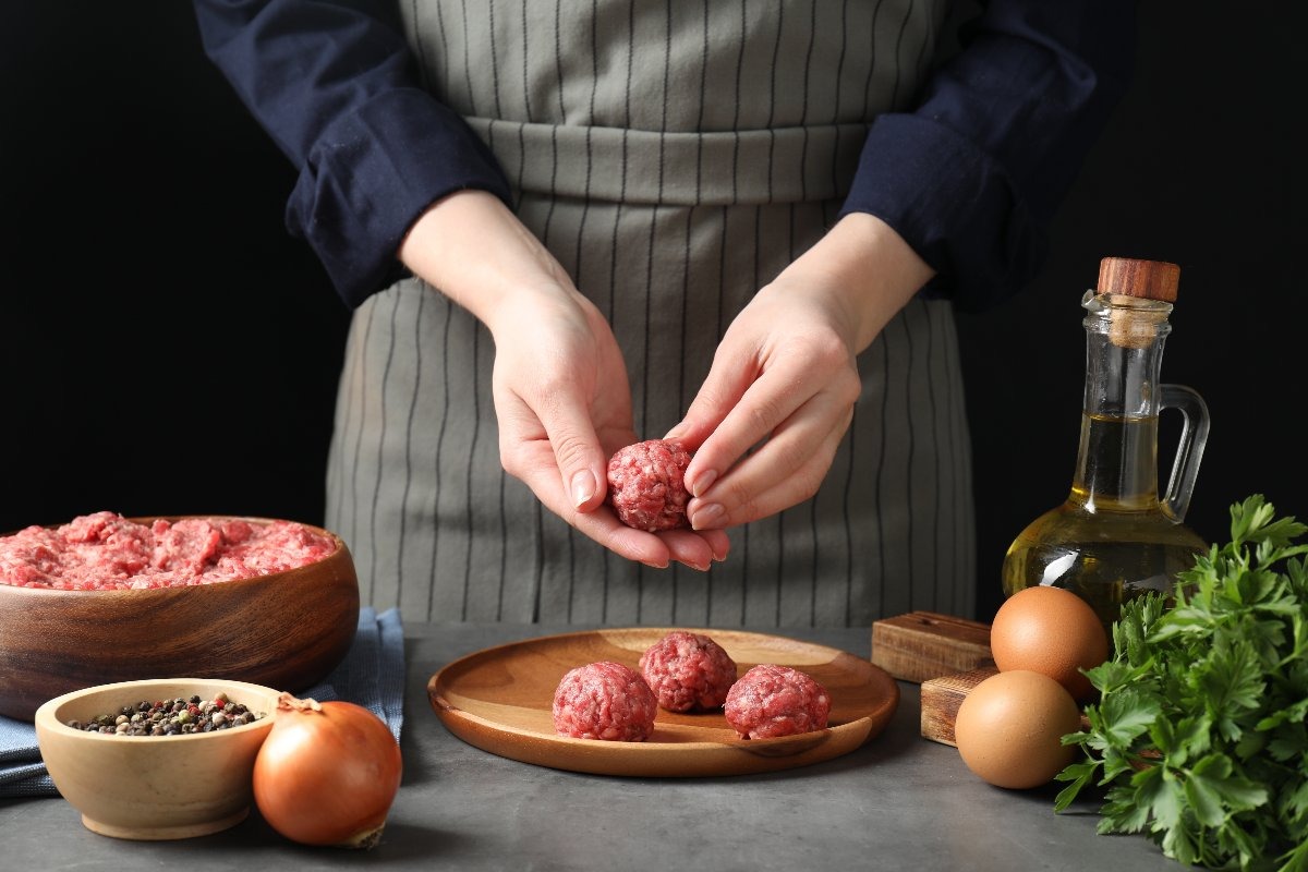 Mani di donna che preparano polpette di carne e le posizionano su piatto di legno