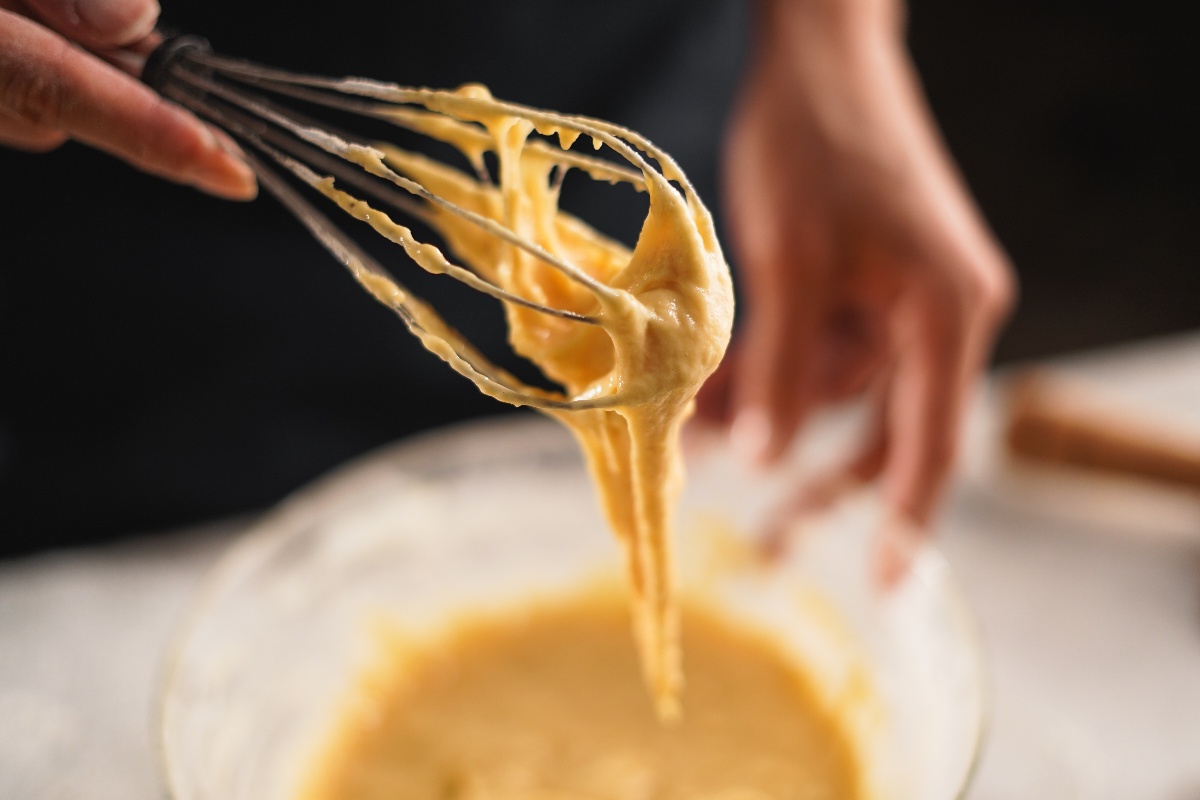 Mano di donna con frusta da cucina che prepara impasto torta