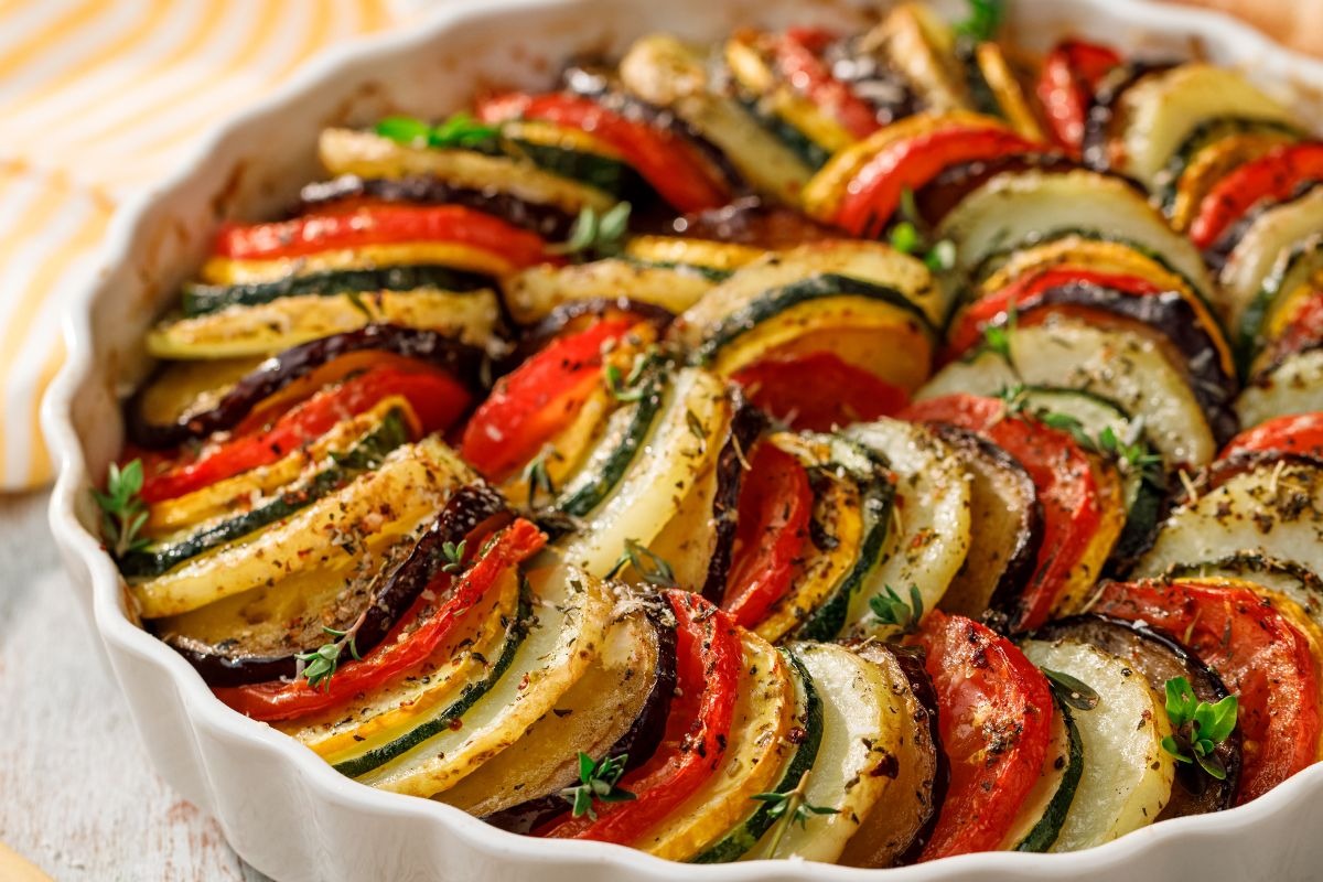 Керамическая форма с нарезанными овощами, уложенными по кругу и приправленными ароматными травами