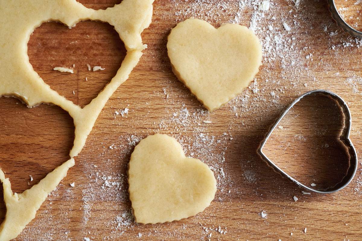 Biscotti di pasta frolla a forma di cuore ancora da cuocere con vicino stampo in metallo