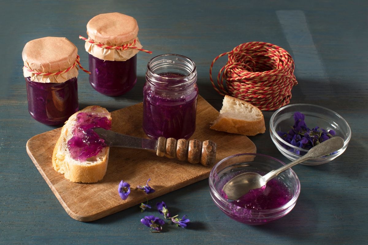 Confettura di colore lilla preparata con violette spalmata sul pane con vicino vasetti di confettura