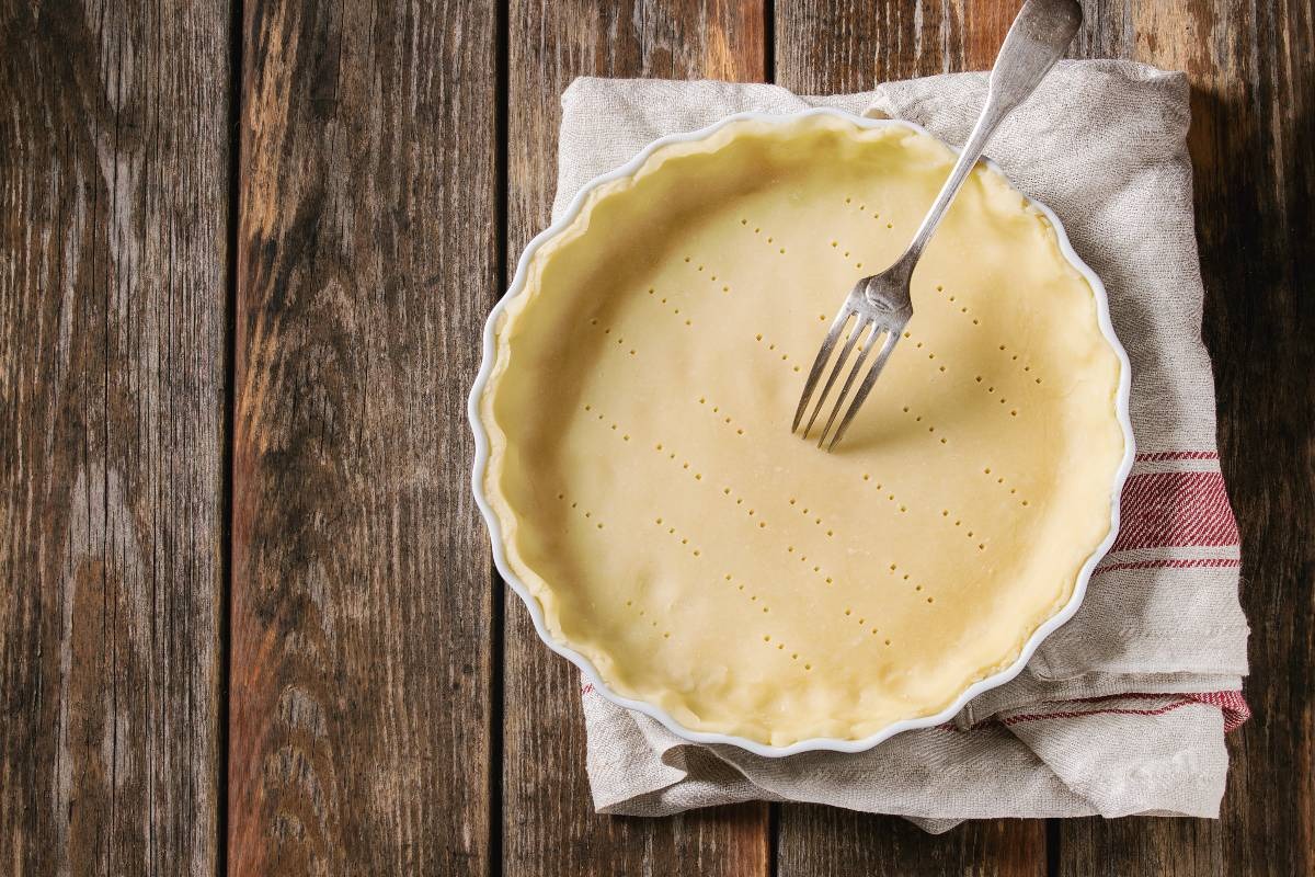 Vista dall'alto pasta frolla nello stampo da crostata bucherellata con forchetta