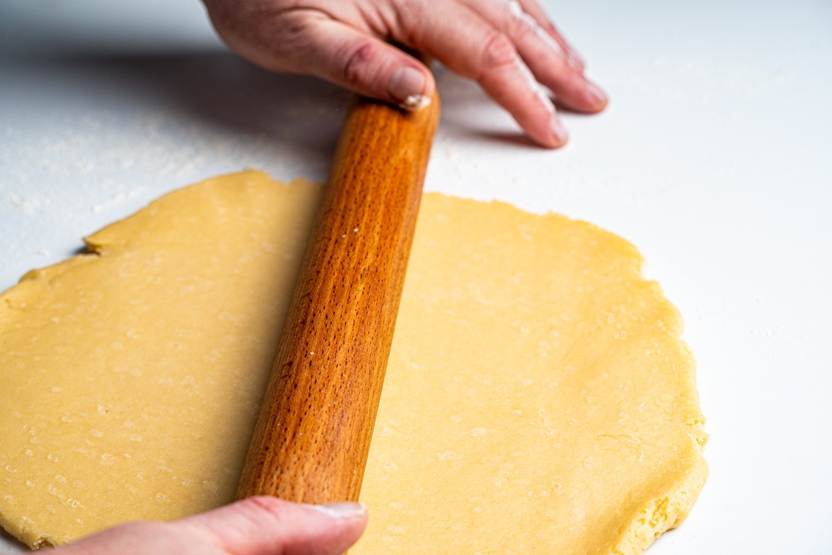 Mani che stendono con il mattarello la pasta frolla