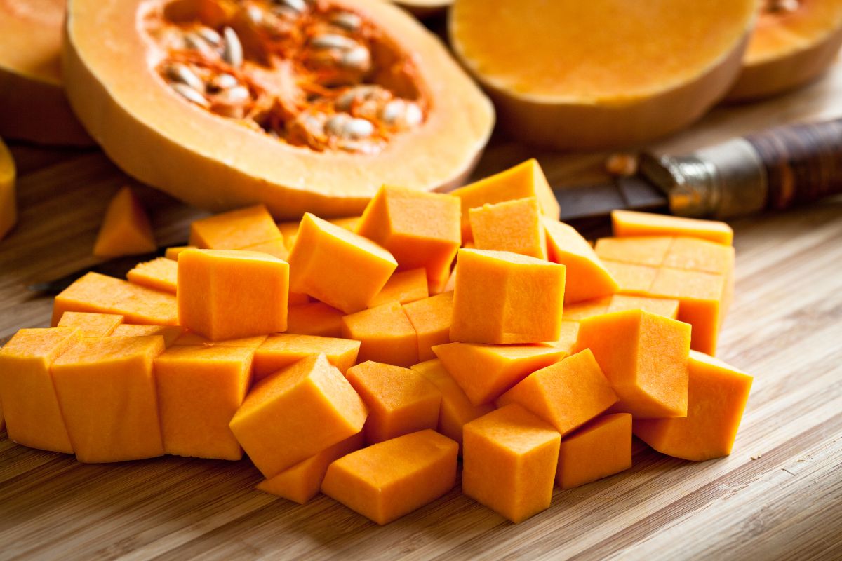 Cubetti di zucca su tagliere di legno con zucca butternut tagliata sullo sfondo