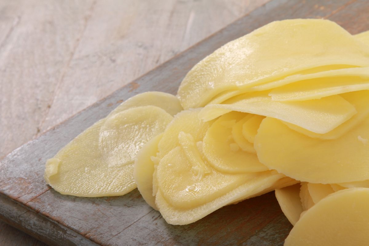 Fettine molto sottili di patate crude su tagliere di legno