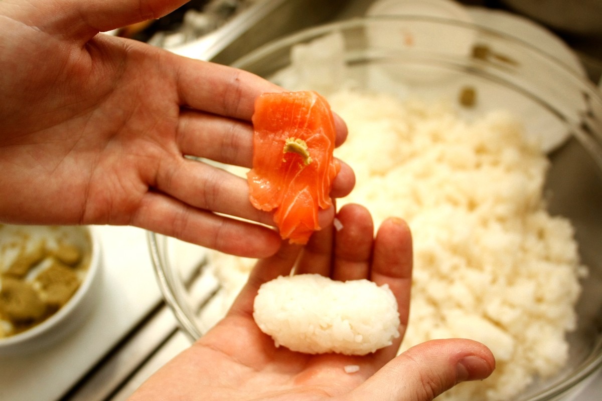 Mani che mostrano le due componenti del nigiri: salmone con wasabi e riso cotto e formato a pallina