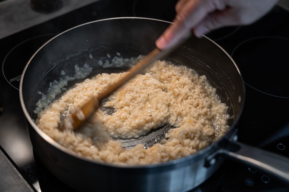 Mano che mescola risotto con cucchiaio di legno