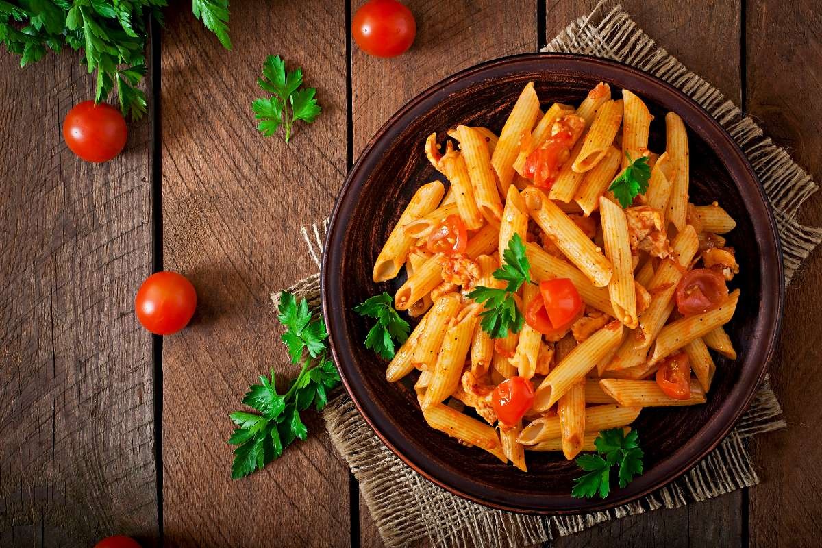 Vista dall'alto piatto di pasta tipo penne condite con sugo a base di pomodoro e pesce