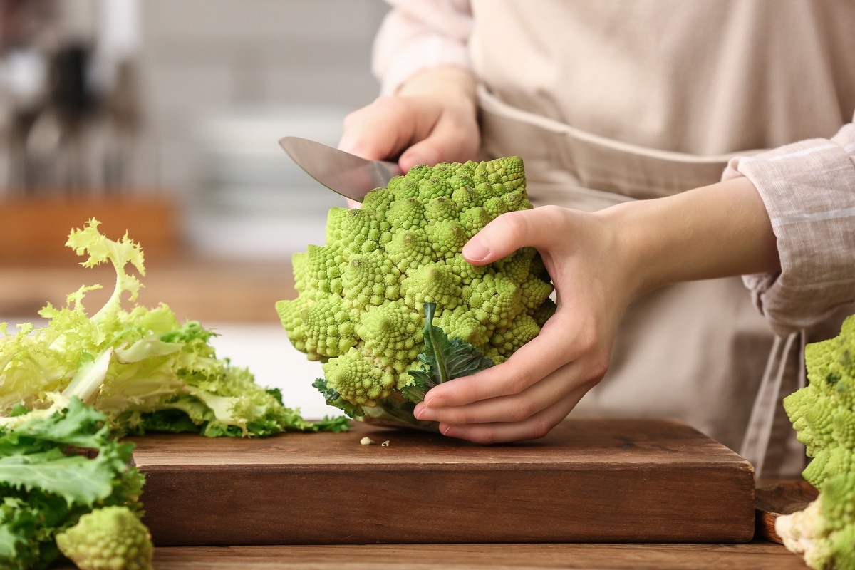 Mani di donna che tagliano broccolo romanesco su tagliere di legno