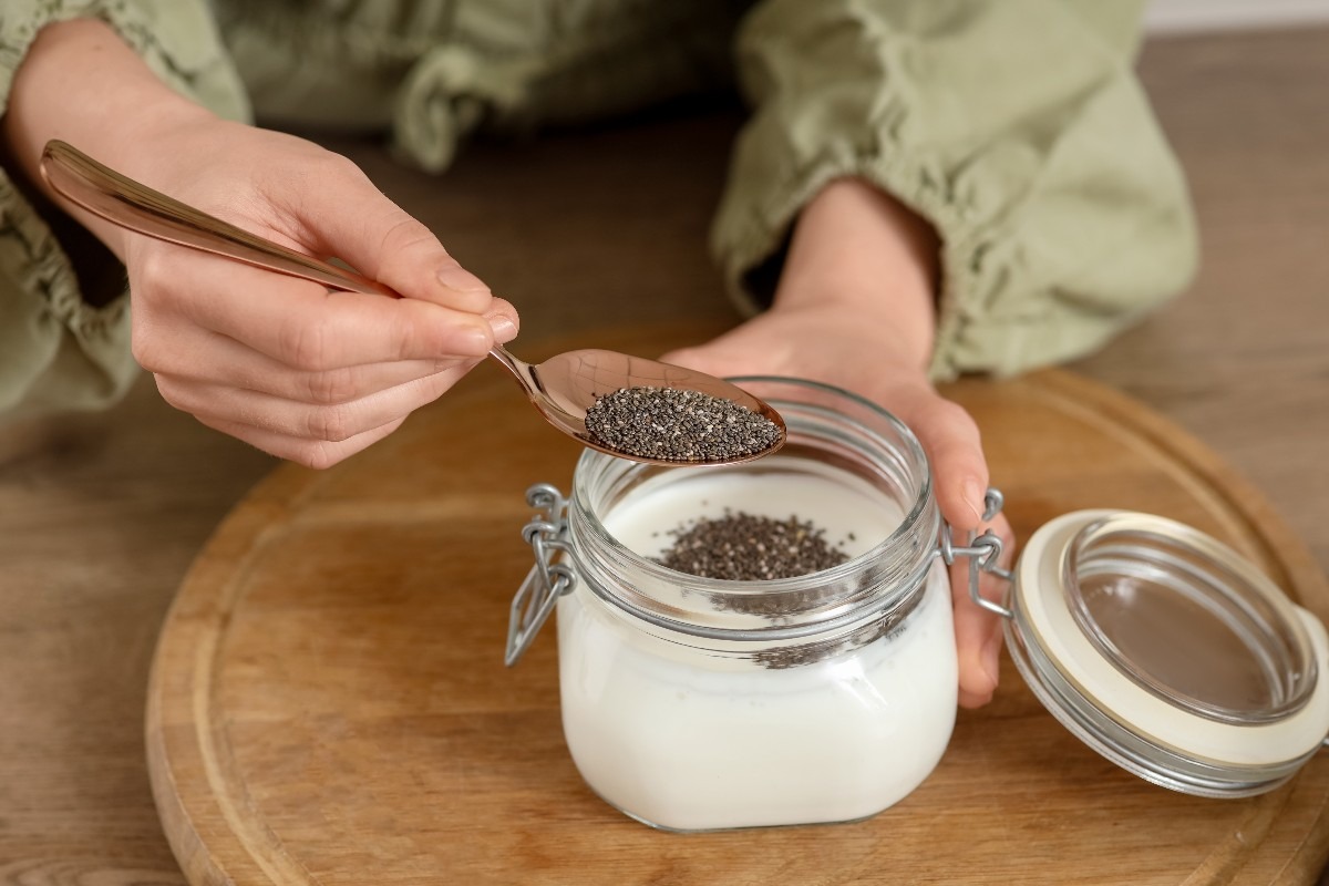 Mani di donna che aggiungono semi di chia a latte in contenitore di vetro