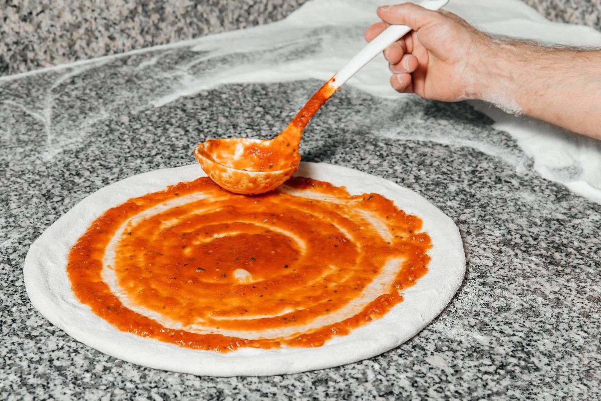Impasto pizza steso a cui viene aggiunta passata di pomodoro