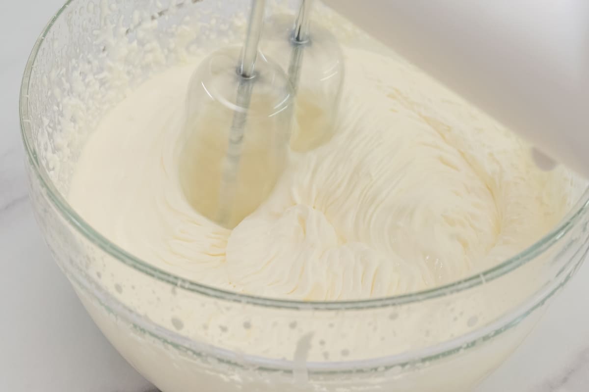 Preparazione crema per cheesecake in ciotola di vetro con fruste elettriche