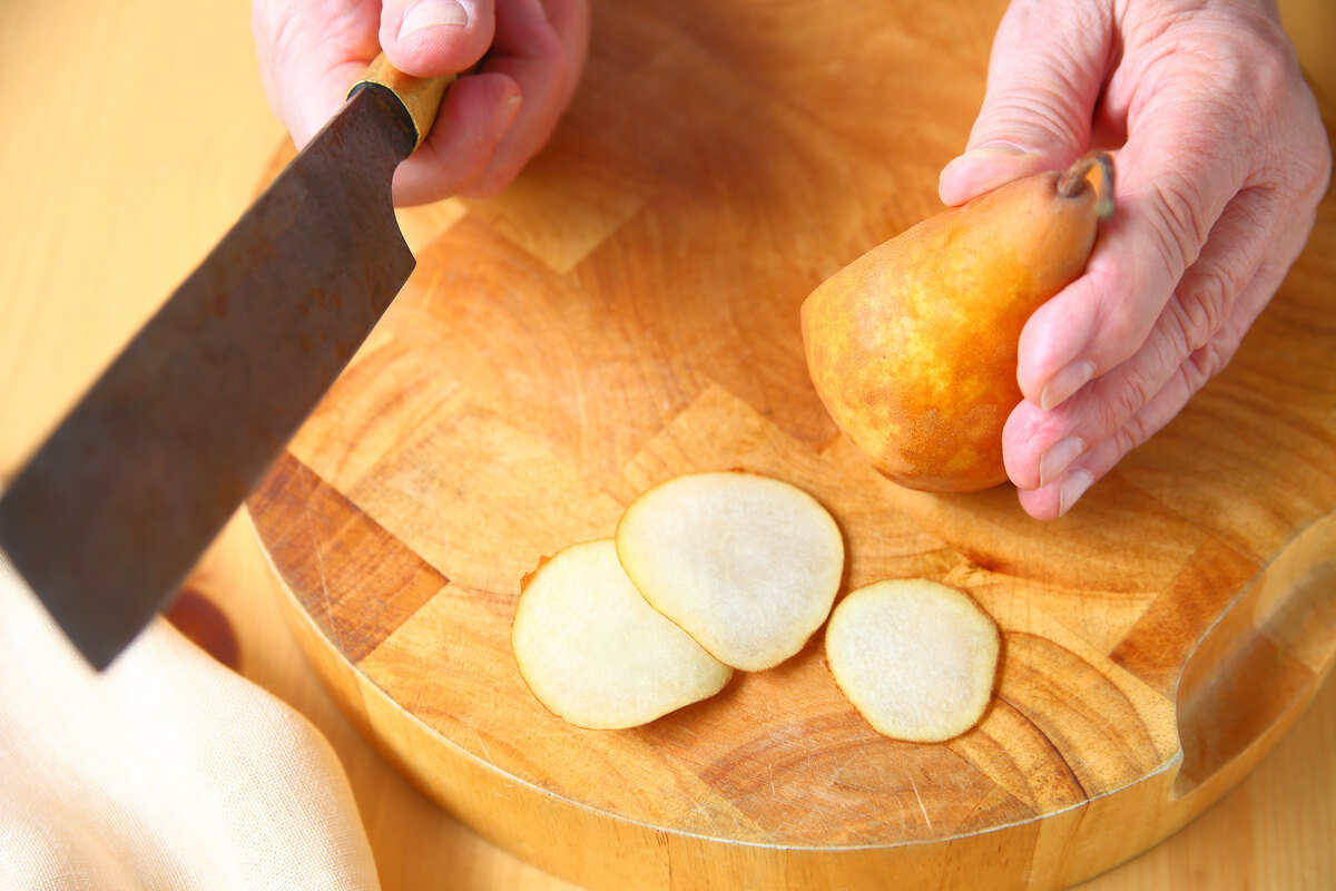 Mani che tagliano a fette sottili una pera su tagliere di legno