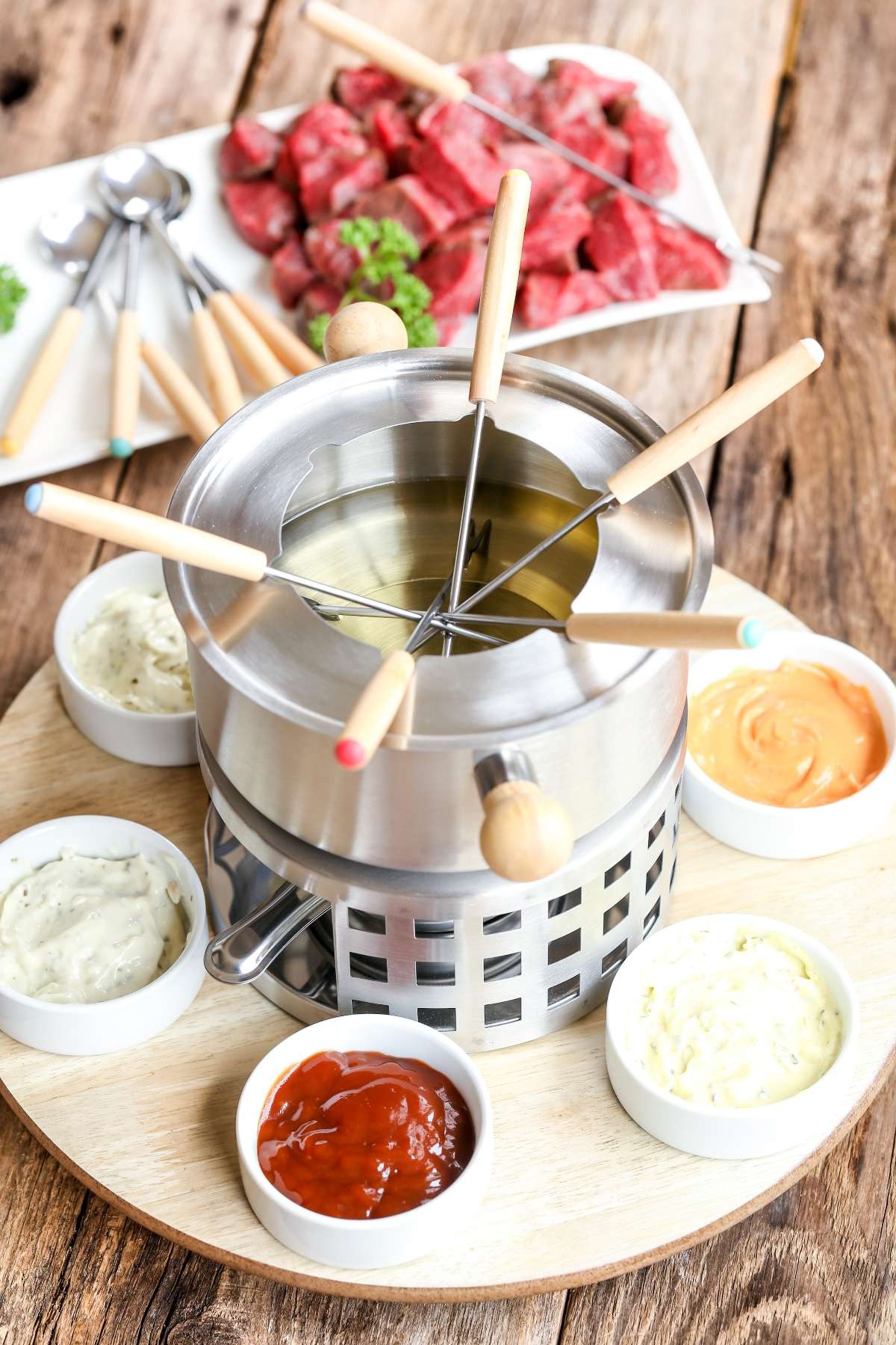 Fornelletto per bourguignonne con olio e attorno salse per servirla. Sullo sfondo, carne a cubetti