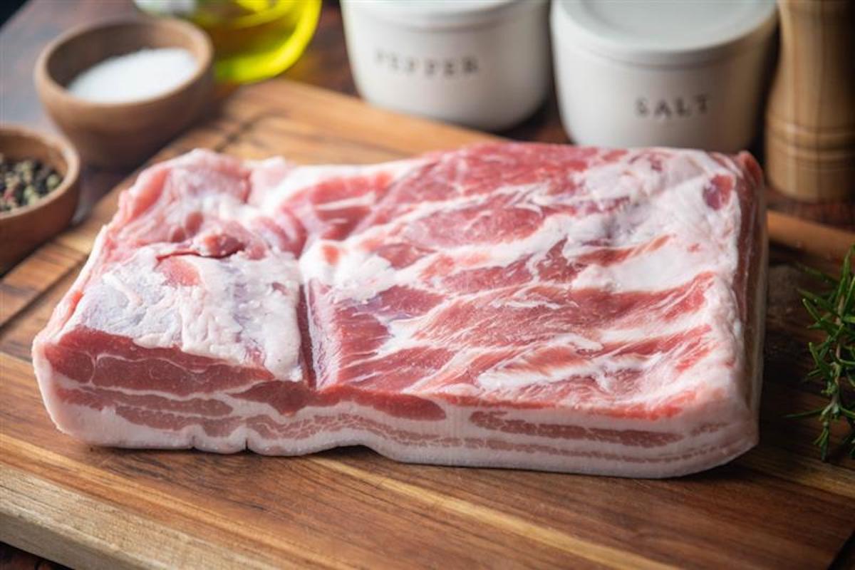 Pezzo di pancetta fresca su tagliere di legno