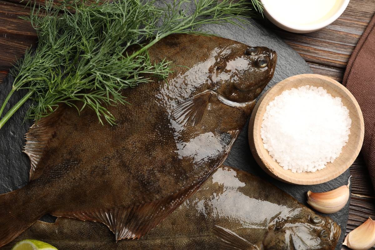Pesce fresco di tipo sogliola su tagliere con sale, aglio e finocchietto